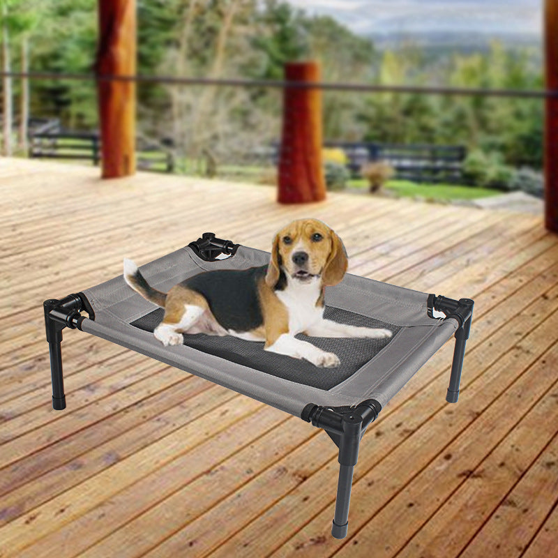 Dog lying on a gray elevated pet bed on a wooden deck with a scenic background.