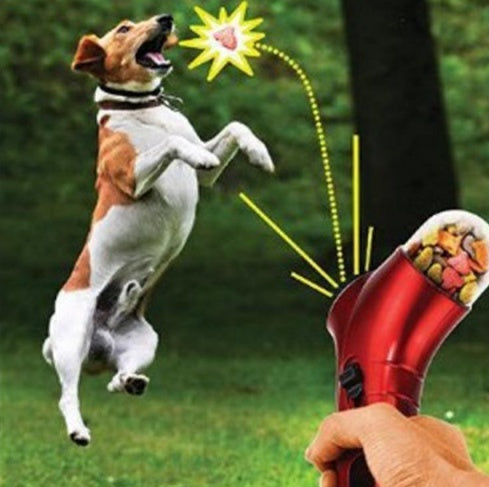 Dog being rewarded with a treat from a red dispenser in a grassy outdoor setting