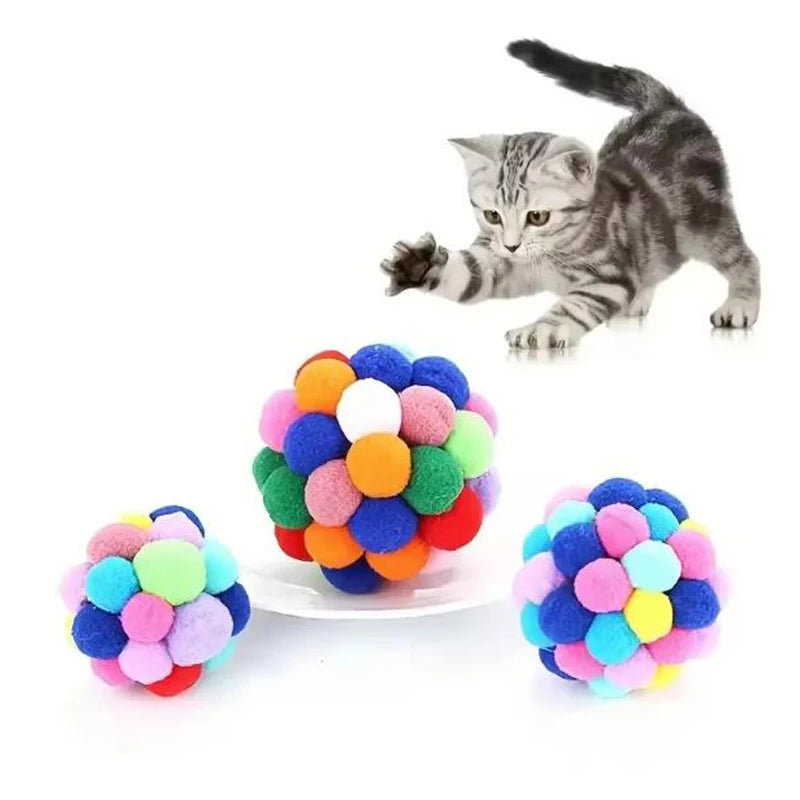 Colorful pom-pom ball cat toy with a cat reaching for it on a white background