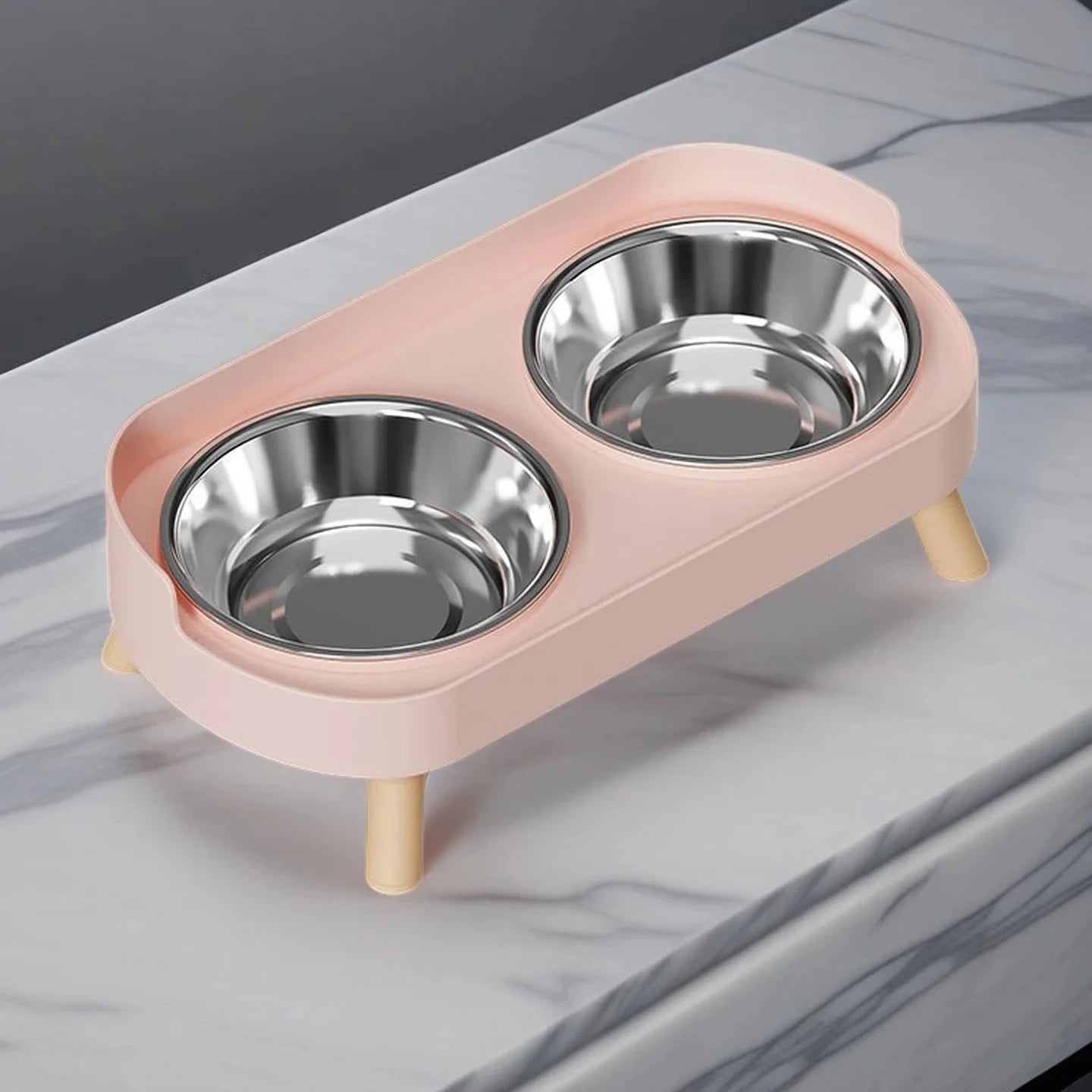 Pink pet feeder with two stainless steel bowls on a marble surface