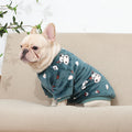 Dog wearing a blue sweater with cartoon designs on a beige couch.