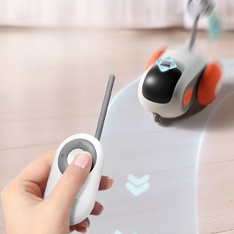 Hand holding a remote control device with a small robot-like device on a light surface.