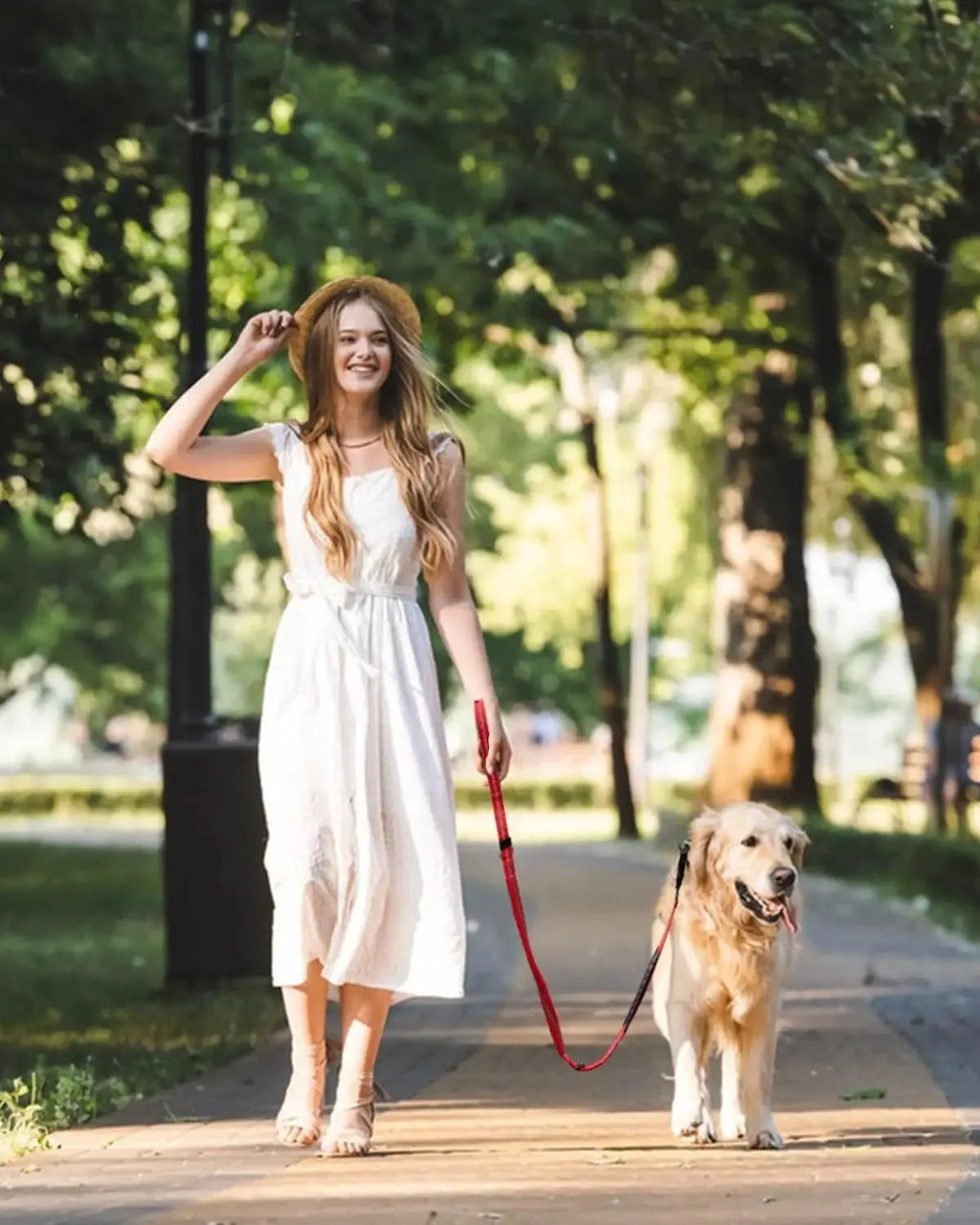 Woman in a white dress walking a dog on a leash in a park.