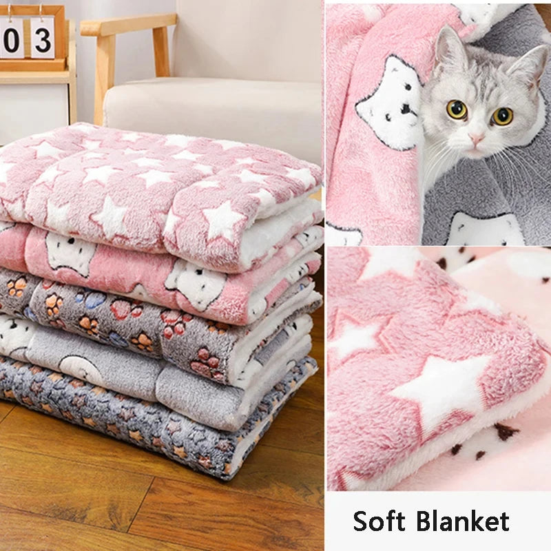 Stack of soft blankets with cartoon designs on a wooden floor, next to a cat on a pink blanket.