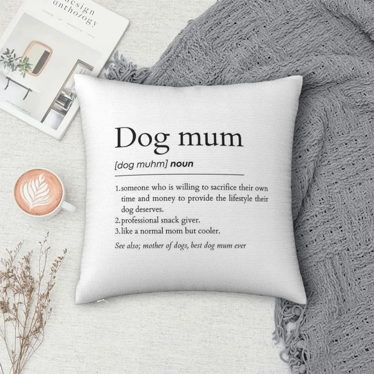 Decorative pillow with 'Dog mum' definition text on a cozy setting with a mug and book.