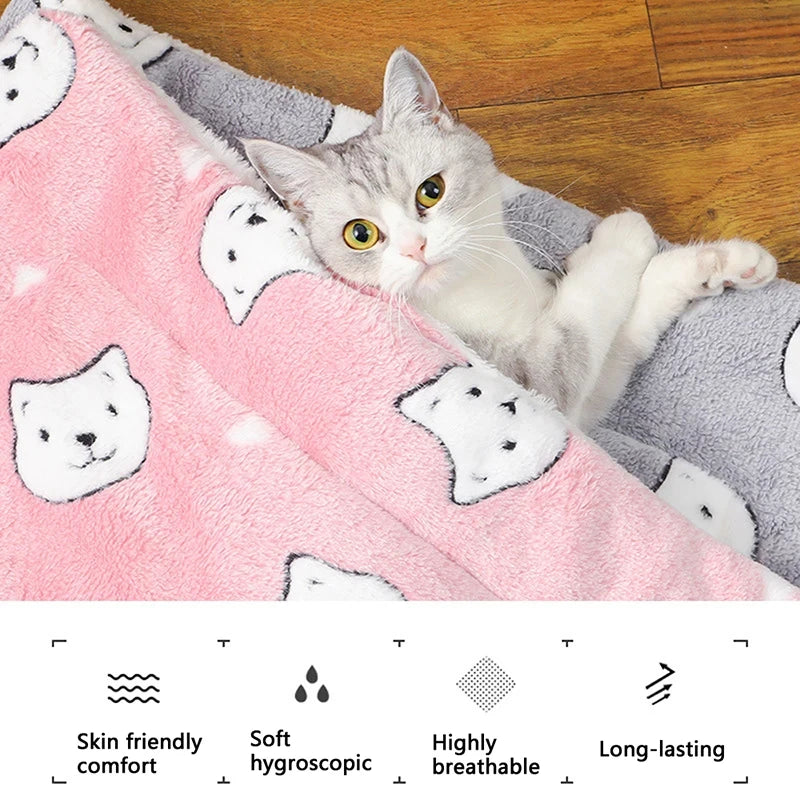 Cat lying on a pink blanket with cat patterns on a wooden floor
